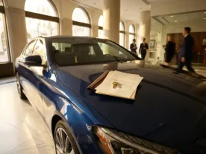 Luxe blauwe sedan in marmeren banklobby met gouden huissleutels en leningdocumenten op motorkap, natuurlijk licht door ramen